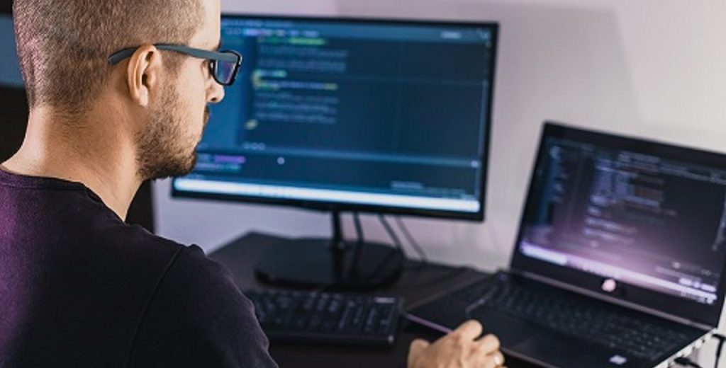 Imagem ilustrativa de homem sentado a frente de dois computadores estudando para as certificações CompTIA.